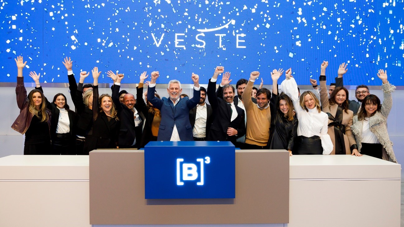 A foto mostra um grupo de pessoas comemorando o aniversário de 15 anos de listagem da Veste com um toque de campainha.
